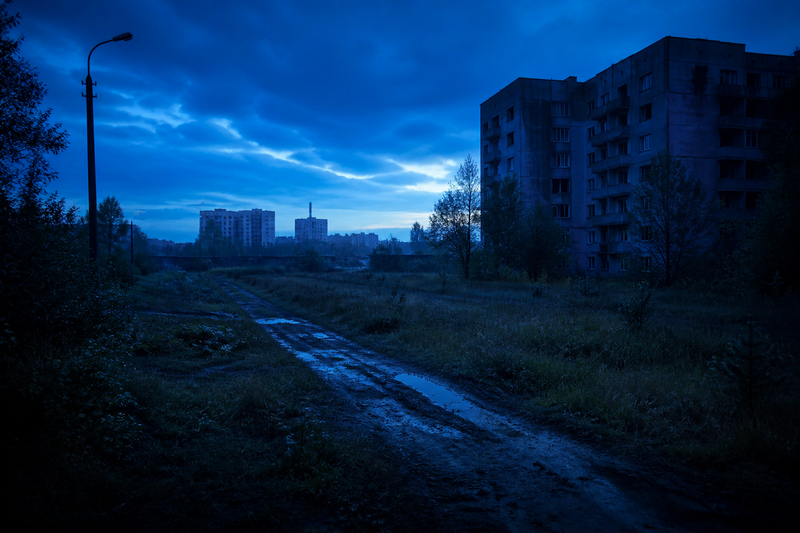 DayZ post-apocalyptic Chernarus landscape at dusk with a survivor holding a rifle near abandoned military buildings